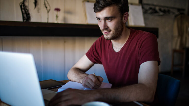 Jeune homme travaillant sur un ordinateur portable et prenant des notes pour son projet immobilier.
