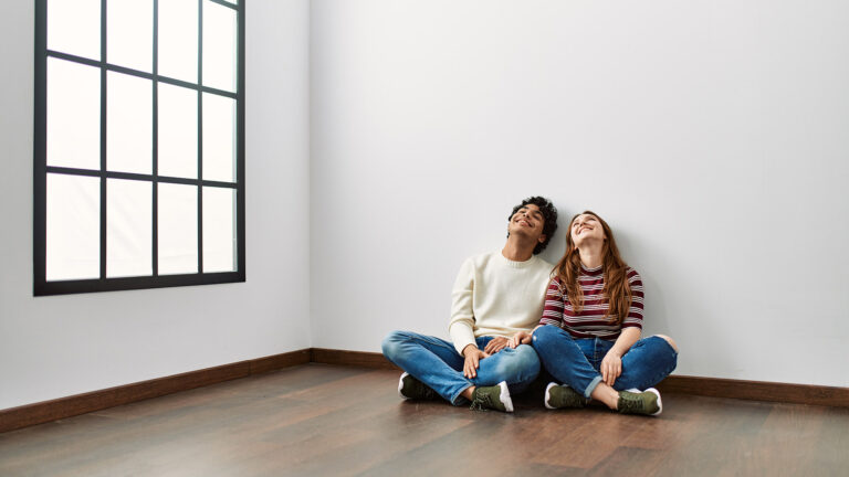 Couple heureux assis sur le sol d'un appartement vide après une location ou un achat.