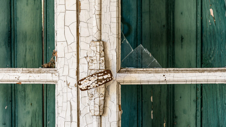 Zoom sur une vieille fenêtre en bois dégradée avec peinture écaillée, symbole d'une passoire thermique.